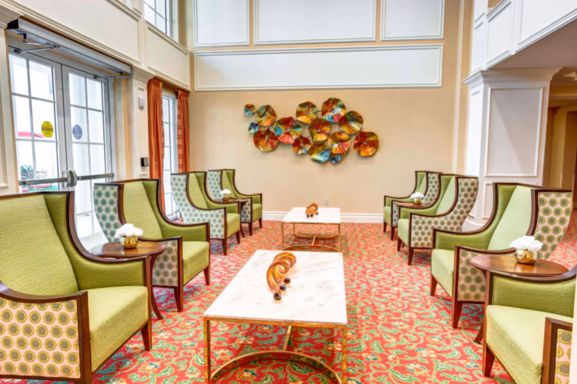 Bright lobby seating area with green chairs and marble coffee tables in a senior living facility.