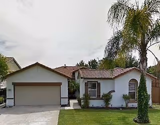 Single-story house with a tiled roof, attached two-car garage, and a well-maintained front lawn with a palm tree and some shrubs.