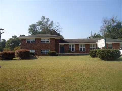 Brick senior living building with a well-kept lawn and shrubs in front.