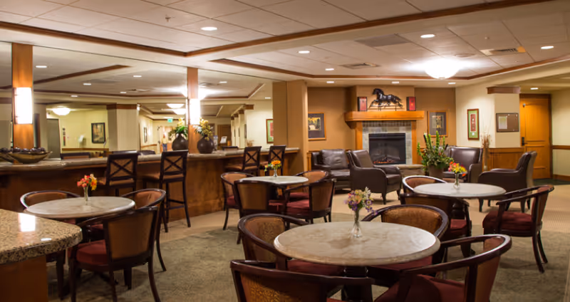 Communal lounge and dining area with round tables, chairs, bar seating, and a fireplace.