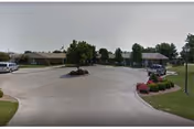 Circular driveway with landscaped island in front of Village Manor building, cars parked to the side.