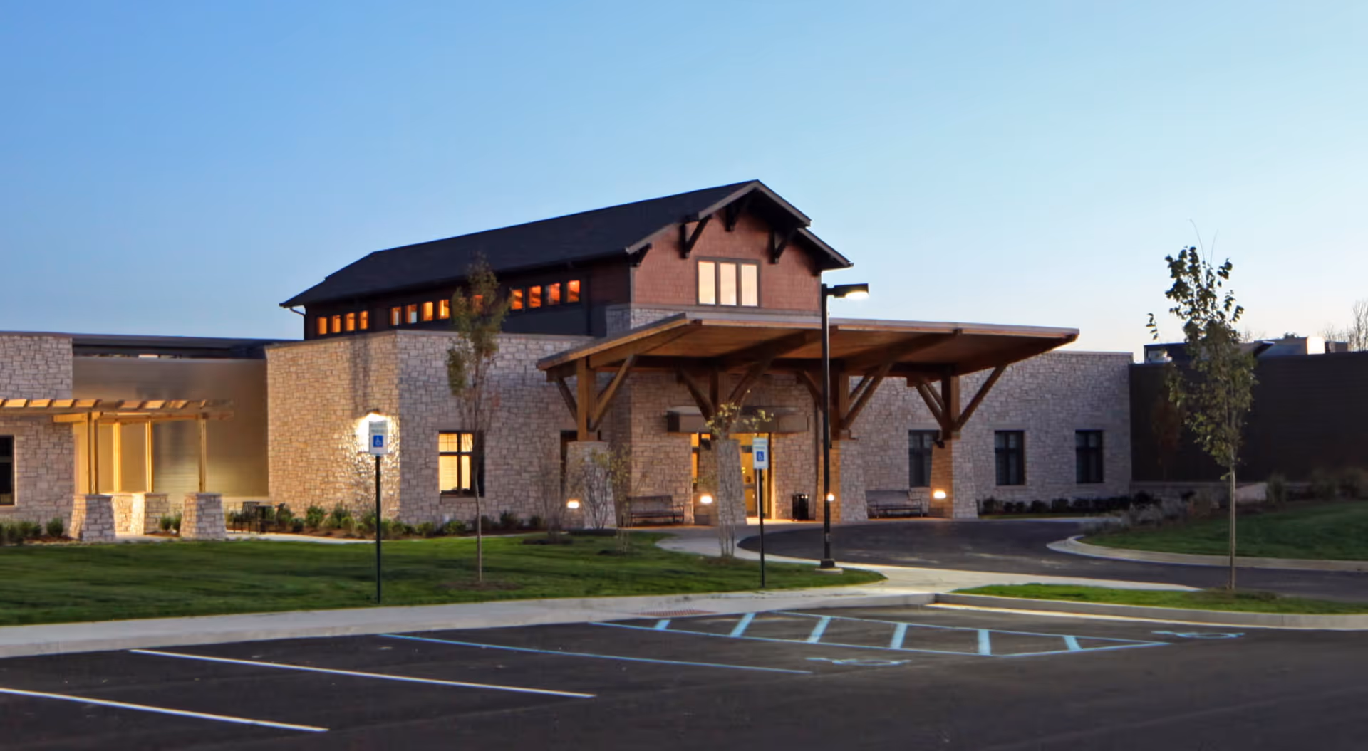 Front exterior of Wellbrooke of Crawfordsville at dusk showing the entrance canopy, stone facade, and empty handicap parking spaces.