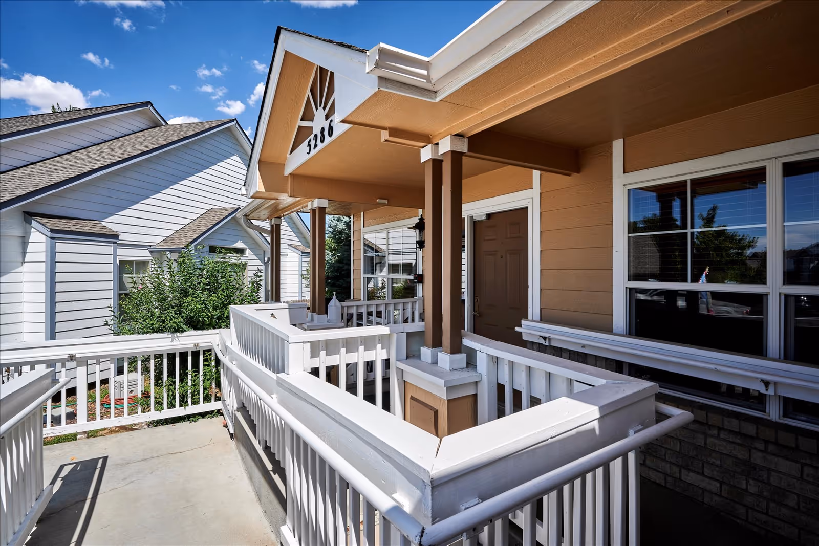 Covered front entrance with white railings and an accessible ramp leading to a brown door beneath a porch labeled 5286.