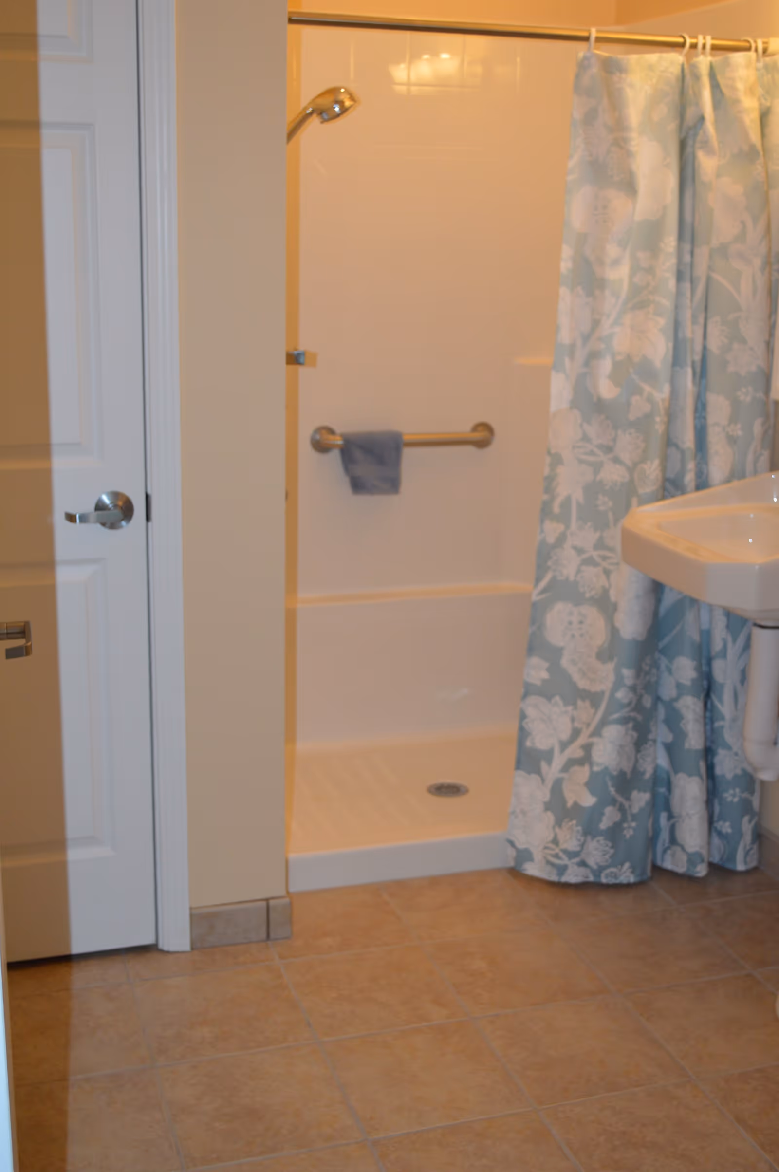 Small bathroom with a walk-in shower with grab bar and floral shower curtain, a pedestal sink, and tiled floor.