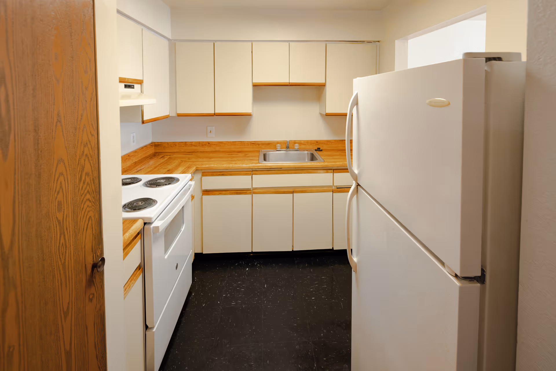 Galley kitchen with white cabinets, wood-effect countertops, a sink, electric stove, and a refrigerator.