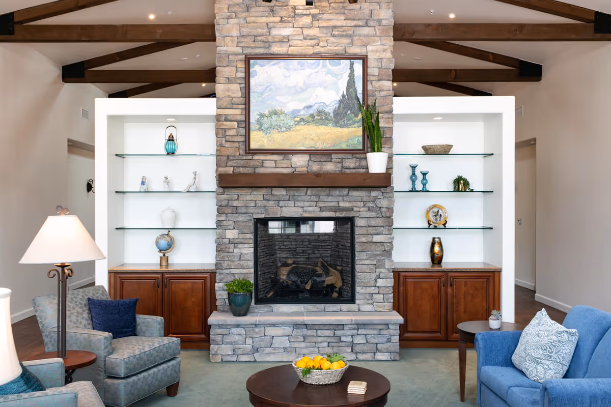 Cozy living room with a central stone fireplace flanked by built-in glass shelves, seating, and a coffee table.