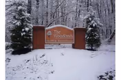 A snow-covered outdoor scene featuring a brick sign for The Woodlands Health & Rehab Center surrounded by trees and bushes also covered in snow.