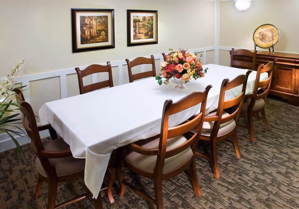 A dining room with a long table covered in a white tablecloth, wooden chairs, and a floral centerpiece.