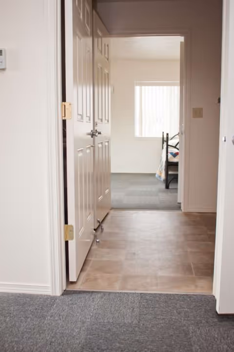 Interior hallway leading to a bedroom with a bed visible through an open door.