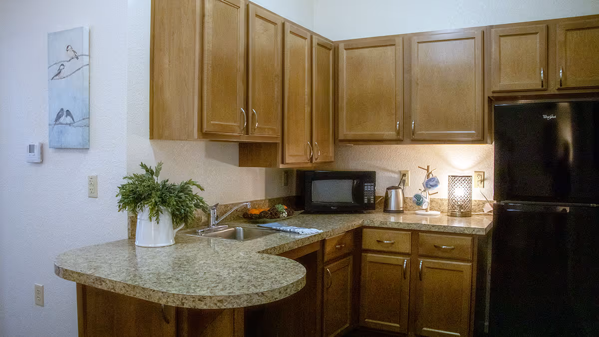 Small kitchen with L-shaped granite countertop, wooden cabinets, a sink, microwave, and a black refrigerator.