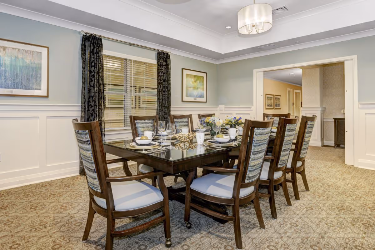 Well-appointed dining room with a large wooden table set for eight, upholstered chairs, and soft overhead lighting.