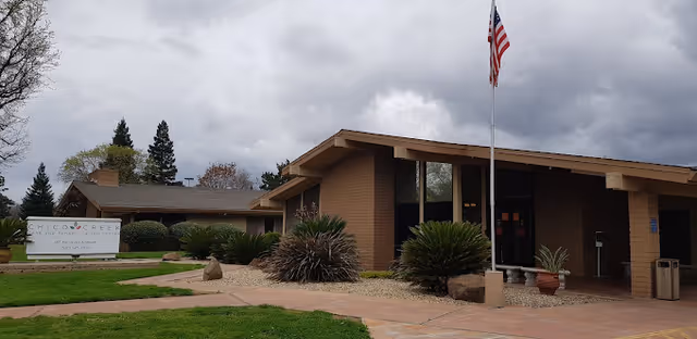 Front exterior of Windsor Chico Creek Care & Rehab building with an American flag, sign, and landscaped entrance.