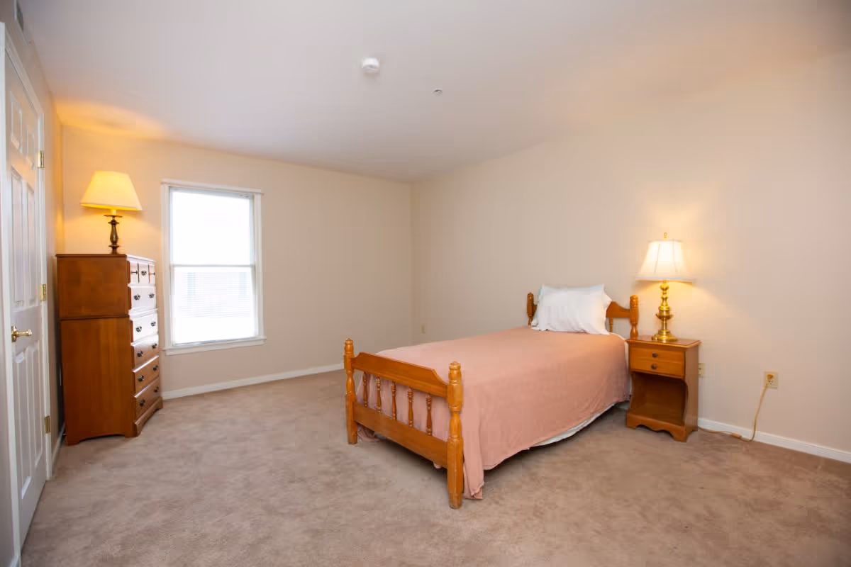 A simple bedroom with a wooden single bed, dresser, nightstands, and warm lamps.