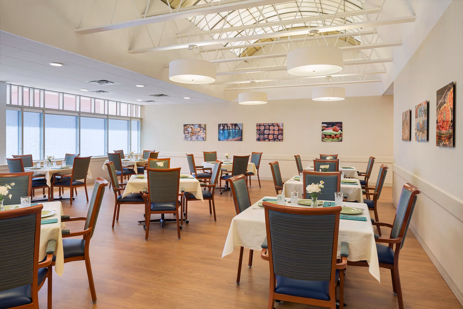 Bright dining room with neatly set tables and chairs under skylights and pendant lights.