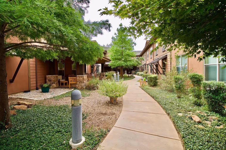 Paved courtyard walkway flanked by landscaping, trees, outdoor lighting, and patio seating between two building wings.
