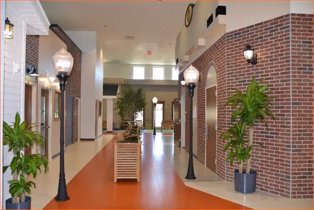 Bright indoor corridor styled like a small street with brick storefronts, lamp posts, potted plants and benches.
