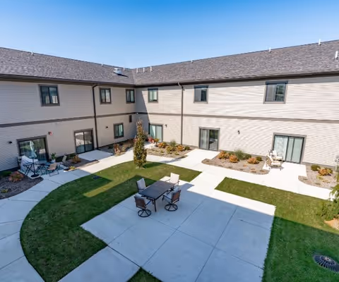 Sunlit interior courtyard of a two-story senior living building with paved walkways, grassy areas and patio furniture.