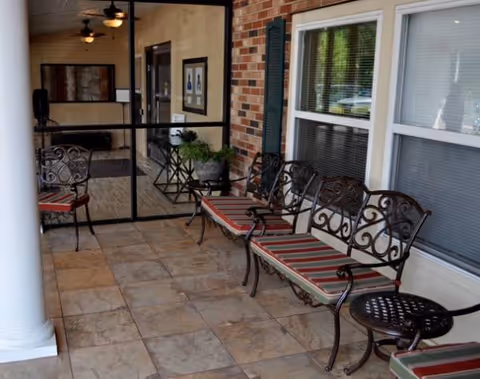 Covered outdoor seating area with wrought-iron benches and striped cushions beside a glass door.