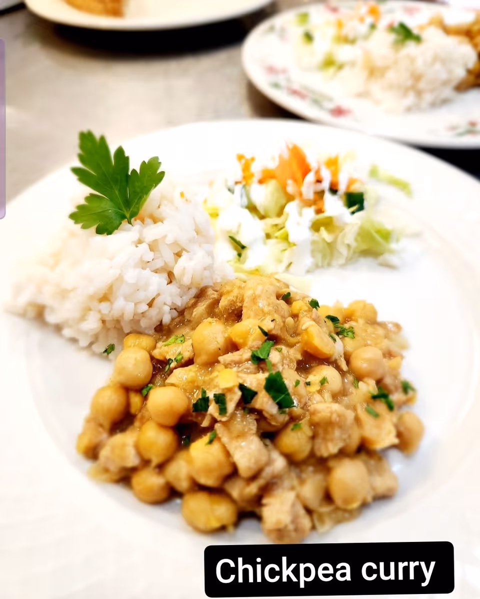 A plate of chickpea curry garnished with chopped herbs, served with a portion of white rice topped with a parsley leaf, and a side of mixed salad with dressing.