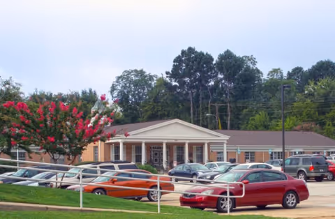 Front view of Dugan Memorial Home, a single-story facility with parked cars and trees.
