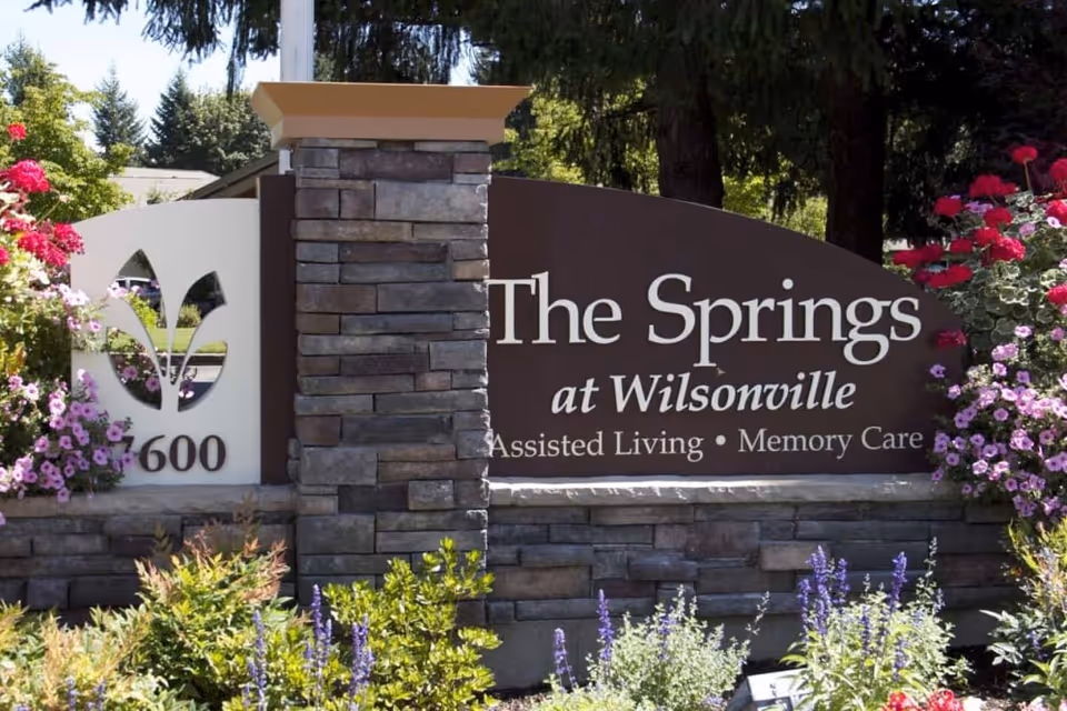 Outdoor stone sign for The Springs at Wilsonville assisted living and memory care facility surrounded by colorful flowers and greenery.