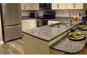 Modern kitchen with granite countertops, stainless steel refrigerator and stove, white cabinets, and a double sink. The kitchen island has place settings with green napkins and plates.