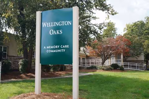 A Wellington Oaks memory care sign stands beside a building entrance.