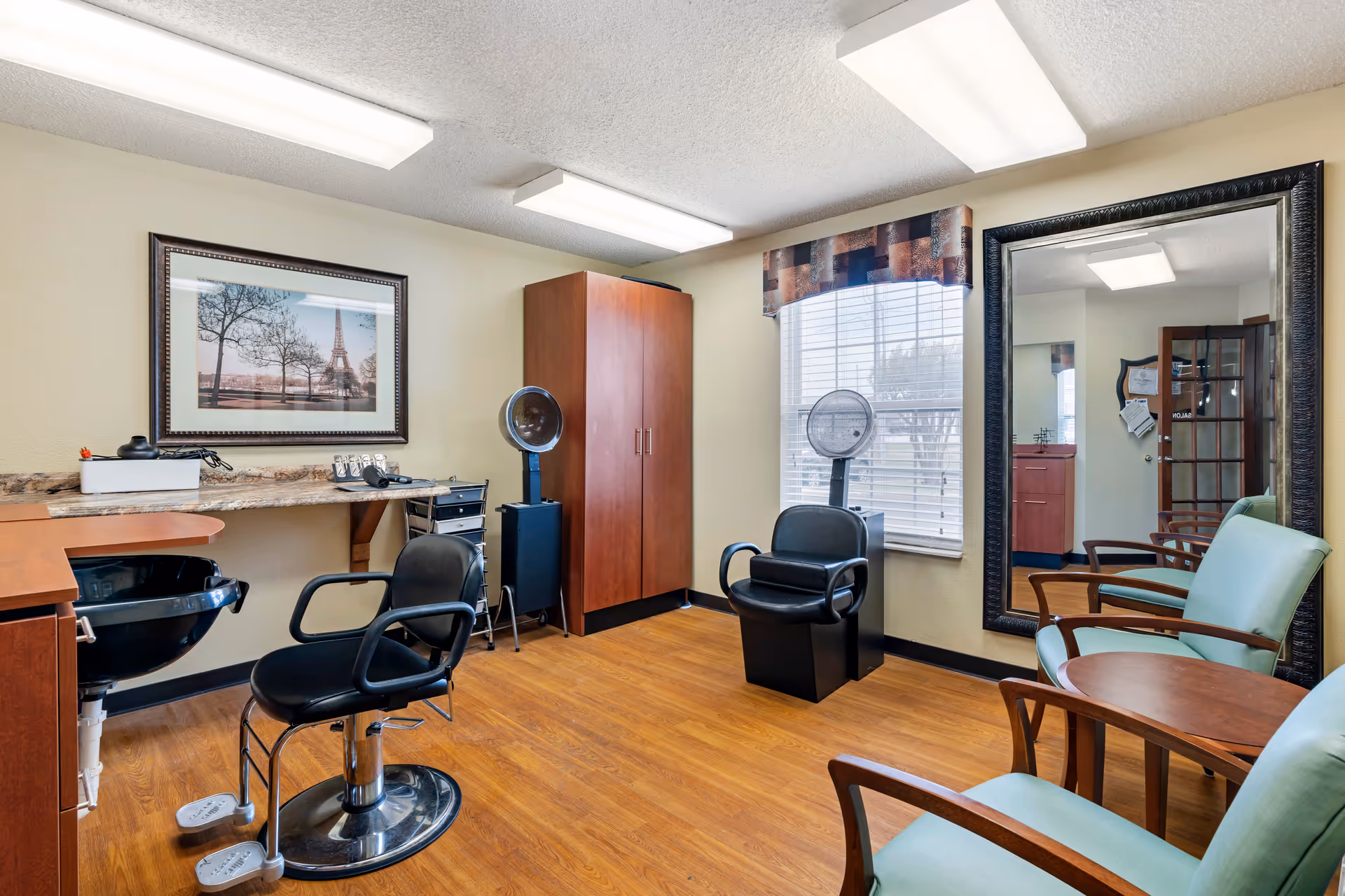 Salon-style interior with hair styling chairs, hooded dryers, a large mirror, and seating for clients.