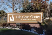 Outdoor sign for Life Care Center of Westminster surrounded by landscaping with trees and bushes in the background under a clear sky.