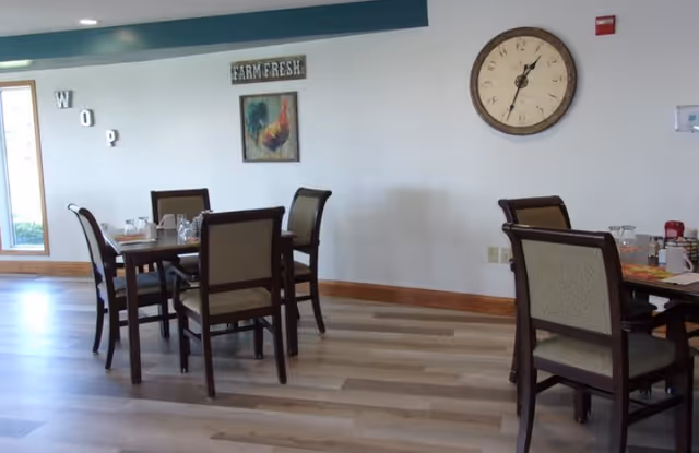 Dining room with wooden tables and chairs, a large wall clock and farm-themed wall art.
