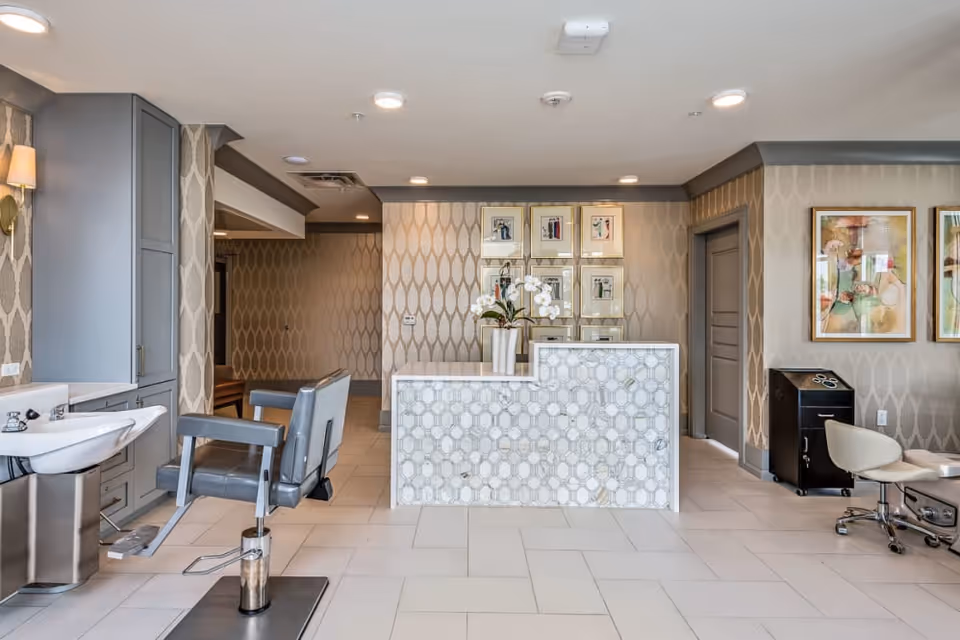 Bright salon reception area with styling chairs, a shampoo sink, and a decorative front desk in a patterned interior.