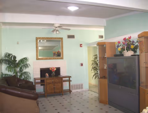 Interior of a senior living home living room with sofa, fireplace, large TV cabinet, and plants.