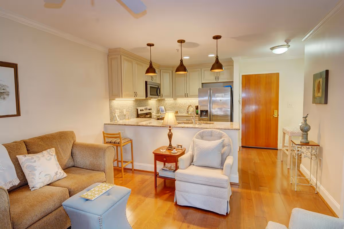 Open living room and kitchen area with a sofa, armchair, small side table, breakfast bar with stools, and hardwood floors.