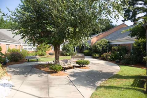 Sunny outdoor courtyard with benches, trees, and a curved walkway near a brick building.