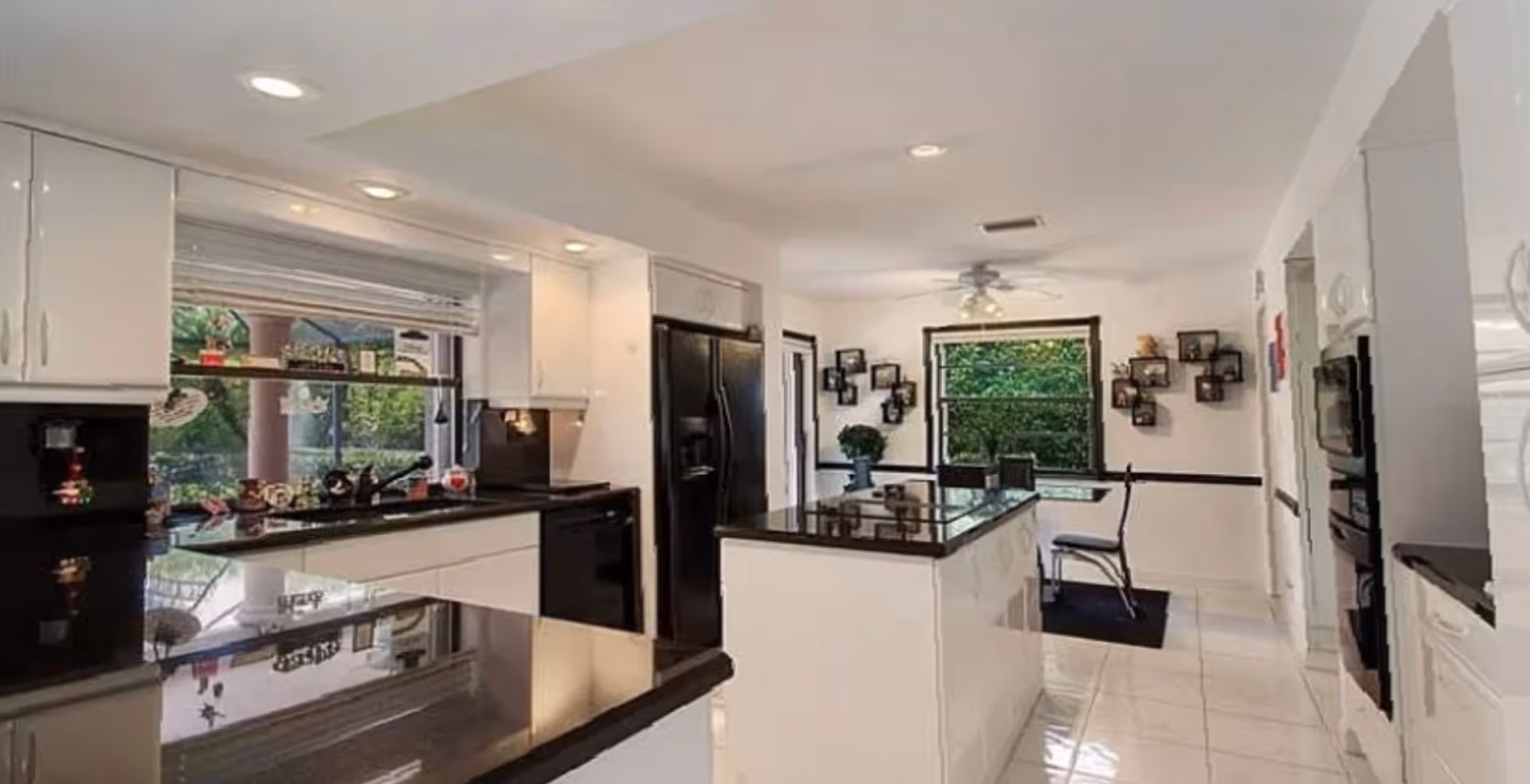 Bright modern kitchen with white cabinetry, black countertops, a central island and a small dining area by a window.