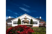 Front exterior of a single-story senior living building with a central fountain and landscaping.