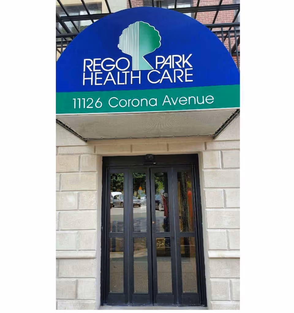 Entrance of Rego Park Health Care with a blue and green awning reading "Rego Park Health Care" and "11126 Corona Avenue" above glass double doors.