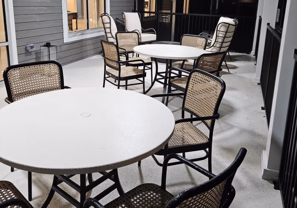 Covered outdoor patio with round white tables and woven rattan chairs arranged on a balcony.