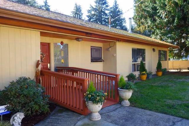 Front exterior of a single-story home with a red porch railing and potted plants.