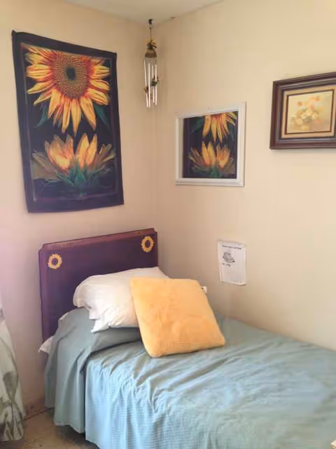 Small bedroom in a senior living facility with a bed and sunflower art.