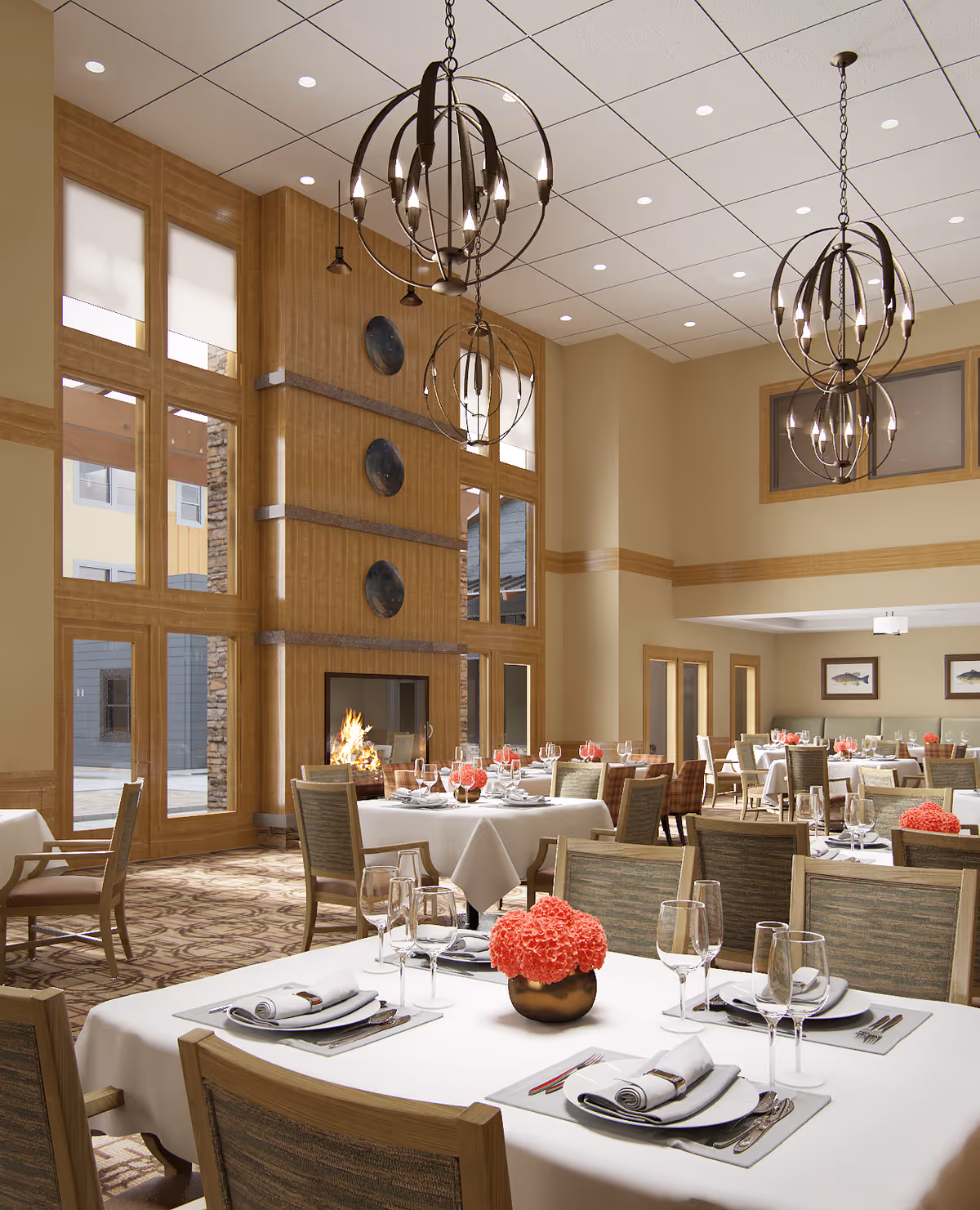 A spacious and elegant dining room with multiple tables set with white tablecloths, napkins, plates, silverware, and wine glasses. Each table features a centerpiece with pink flowers in a small vase. The room has large windows allowing natural light to enter, a lit fireplace, and modern spherical chandeliers hanging from the ceiling. The walls are decorated with framed artwork and wood paneling accents.