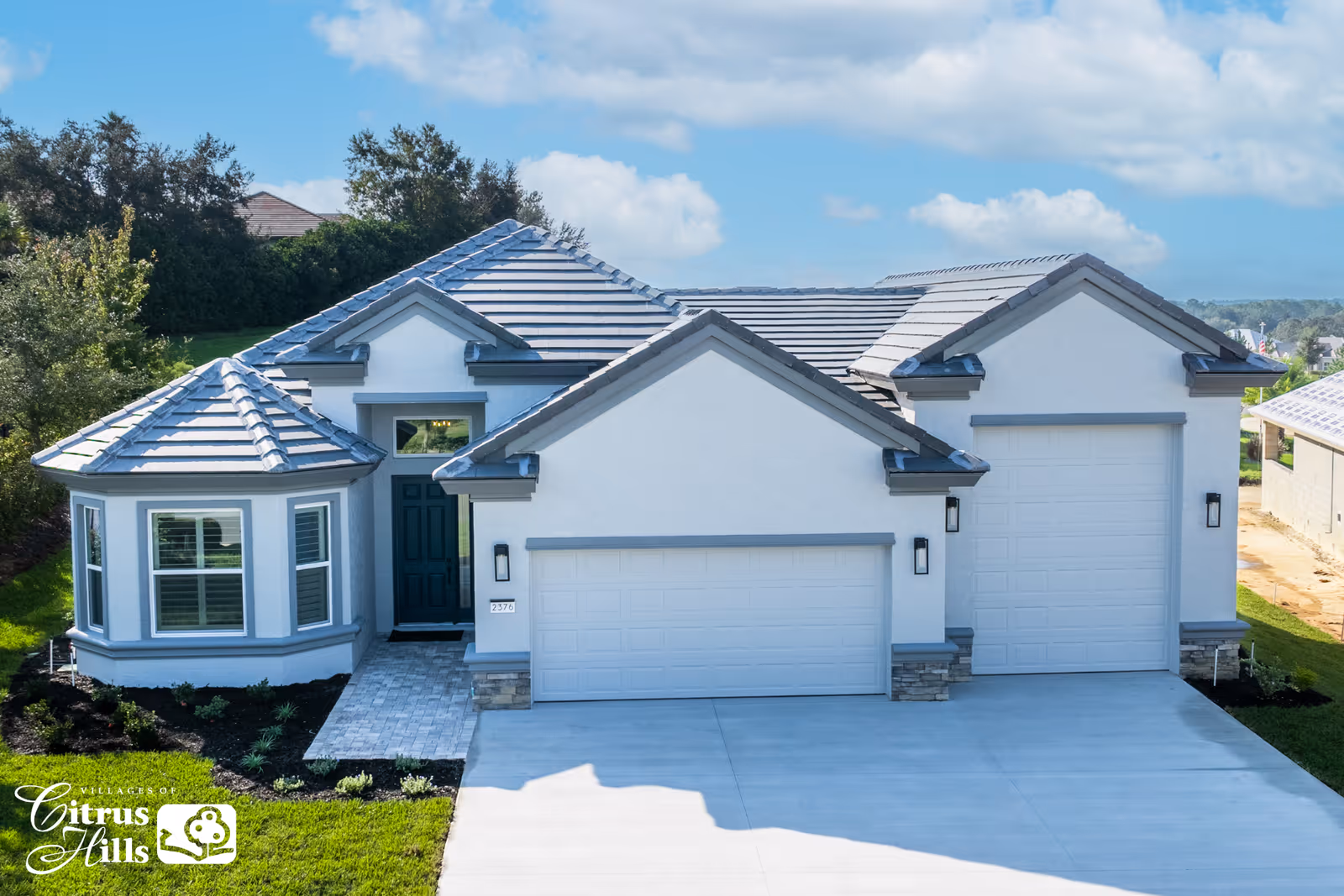 Front exterior of a modern single-story house with a three-car garage, tiled roof, and driveway.