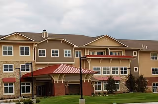 Exterior view of The Regent senior living facility with tan siding and red awnings, entrance visible.