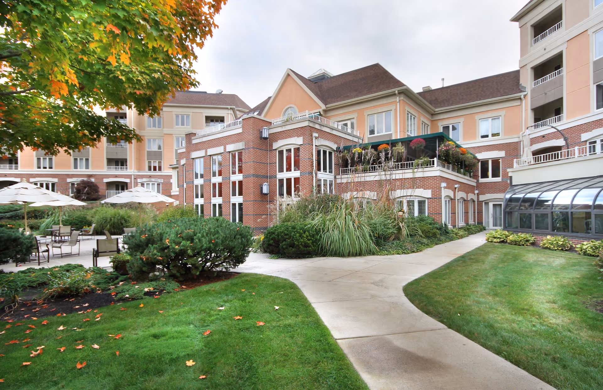 Courtyard and entrance of a multi-story senior living building with a brick facade, landscaped lawns, and outdoor seating.