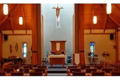 Interior chapel with pews facing an altar and hanging crucifix.