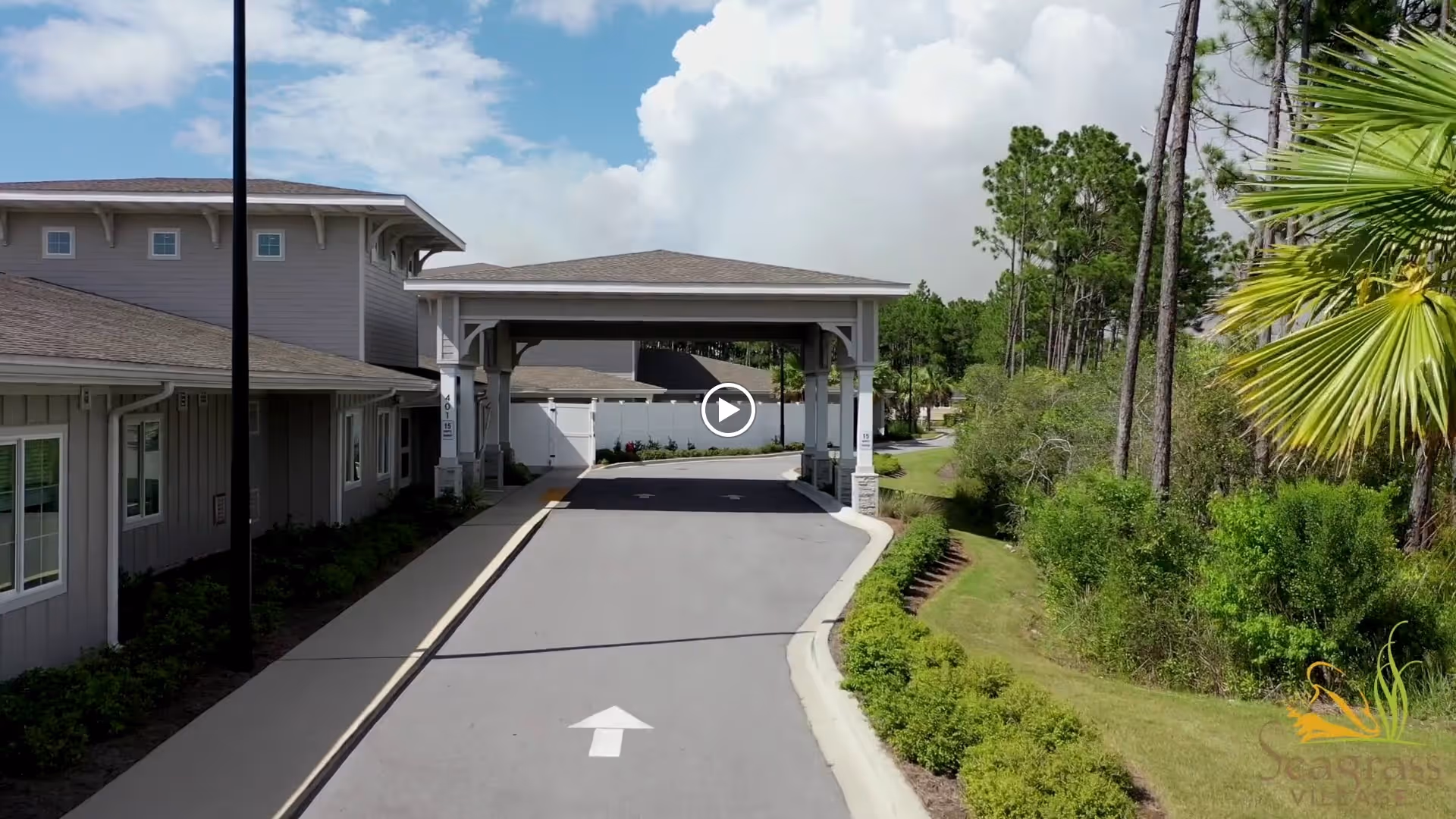 Entrance driveway of The Landing of Panama City Beach facility with a covered drop-off area, surrounded by landscaped greenery and trees under a partly cloudy sky.