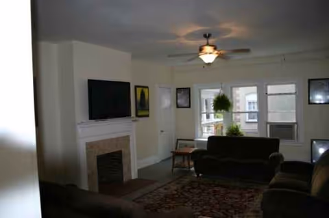Living room with sofas, a fireplace, TV, ceiling fan, and large windows.