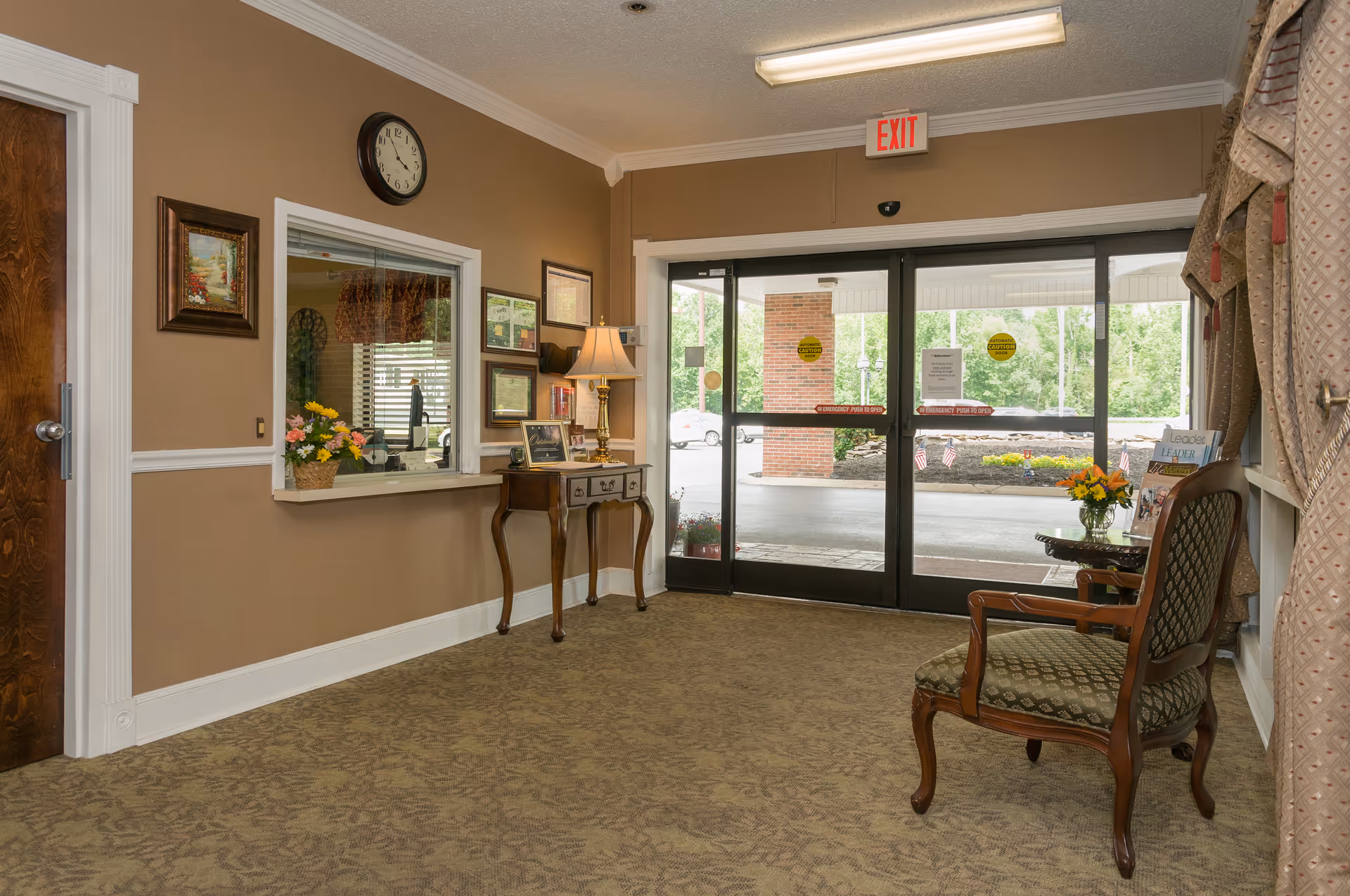 Reception lobby with a service window, table and chairs, and glass automatic entrance doors.