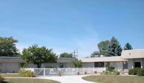 Single-story senior living facility exterior with white railing and surrounding trees.