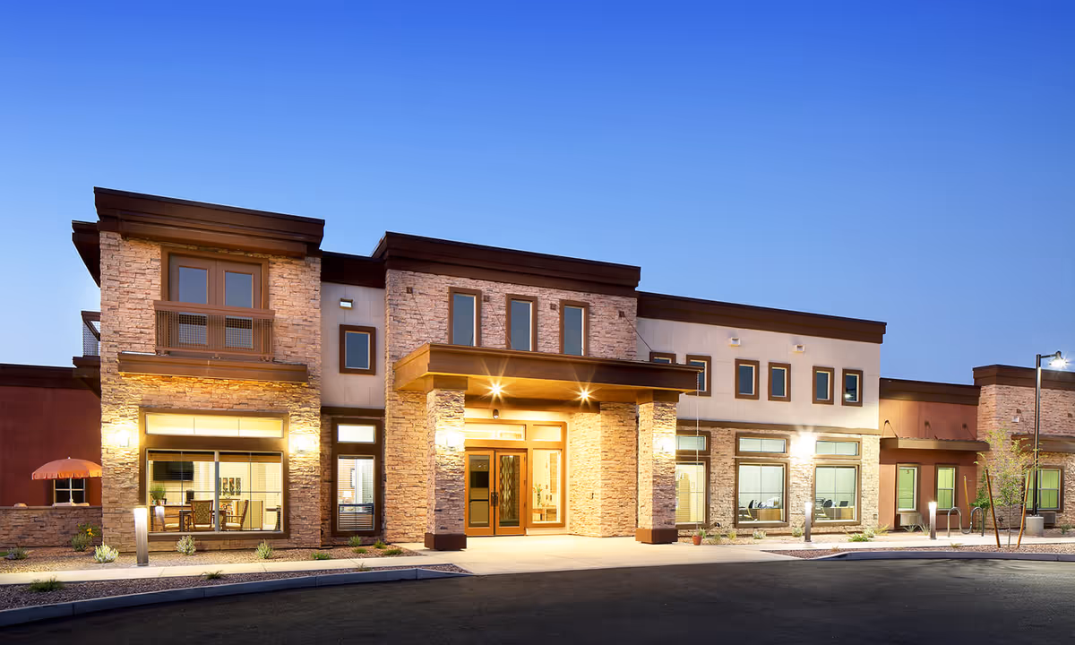 Exterior view of a modern senior living facility building named Sky Vista during dusk, featuring stone and stucco facade, large windows, and warm entrance lighting.